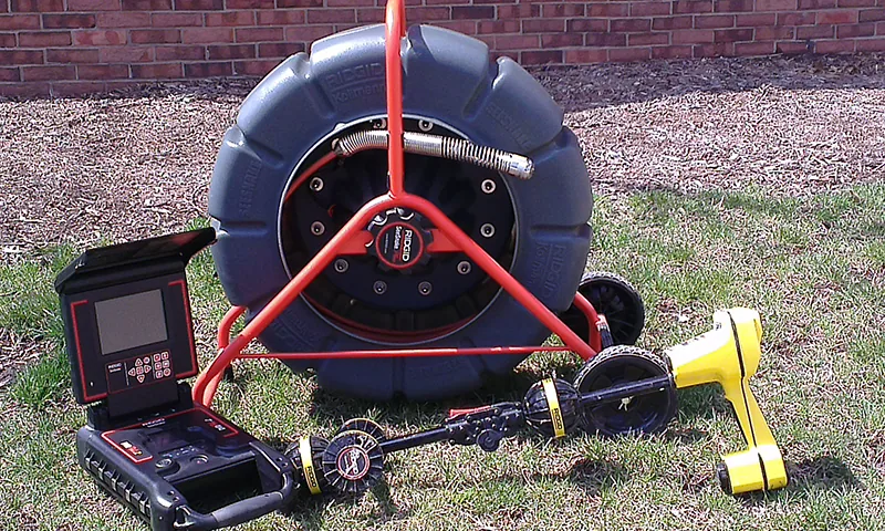 Mint Plumbing's CCTV drain camera reel and monitor with a locator, set up on the grass beside a brick house