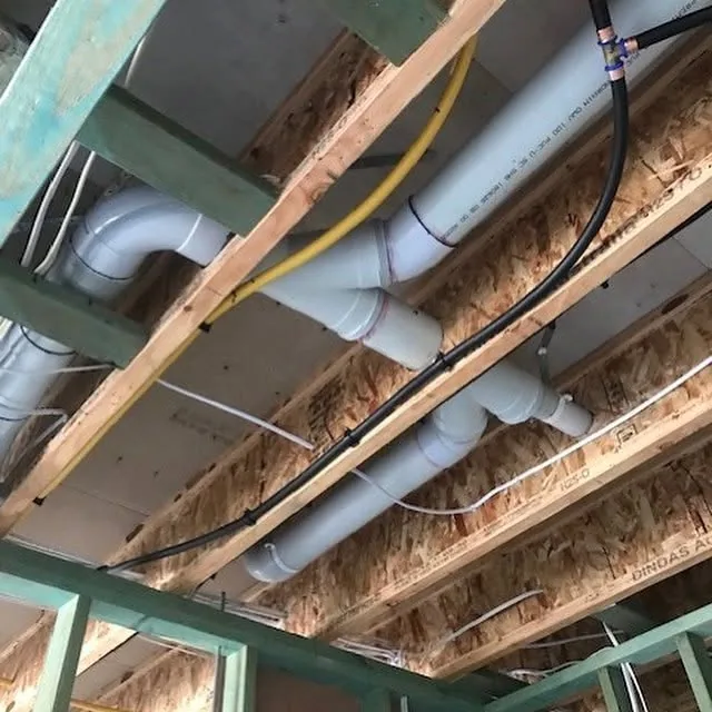 Under-floor rough-in on a new home: white PVC drainage, a yellow gas line and water pipes run through the joists