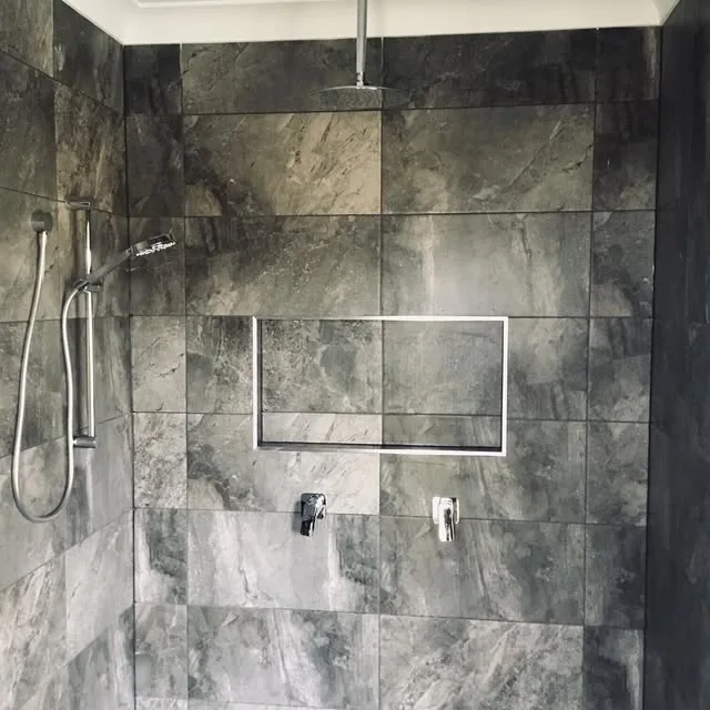 A finished shower in grey stone-look tiles with a rain head, hand shower and wall niche